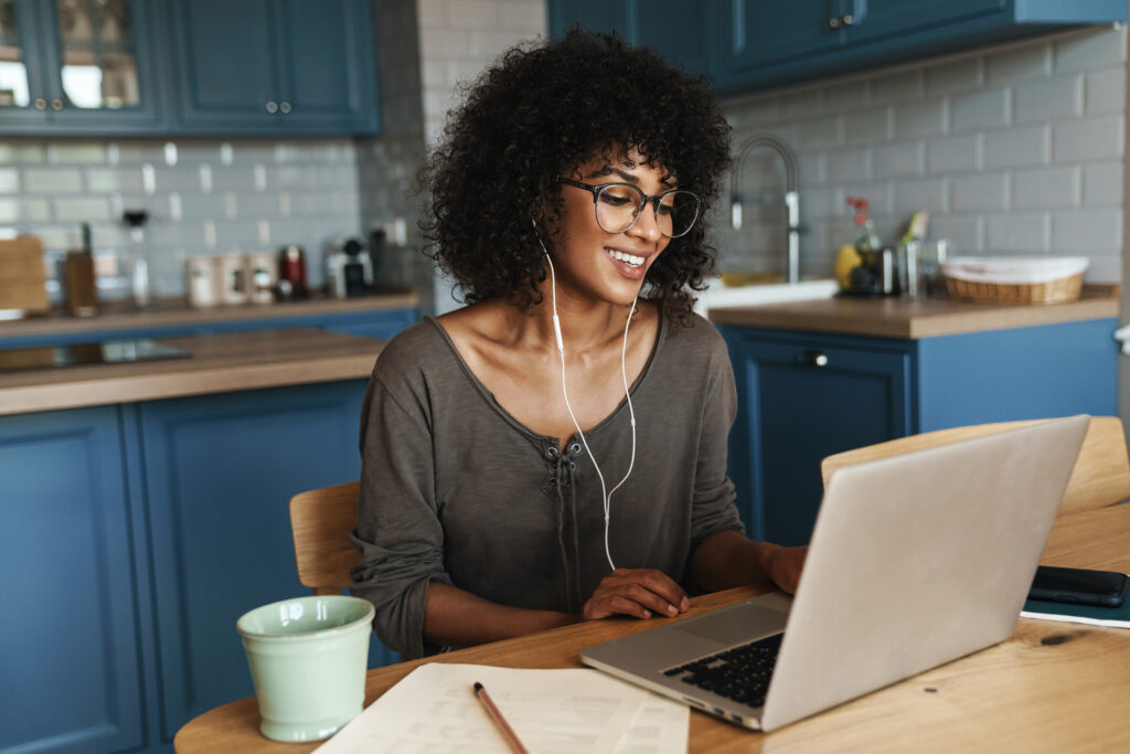 Lady on laptop in kitchen smiling at screen with headphones in